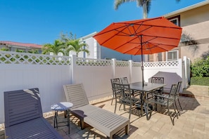 An outdoor patio with a table and chairs, a lounge chair, and a large orange umbrella.