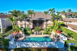 A multi-story hotel with a swimming pool, palm trees, and a covered patio area.