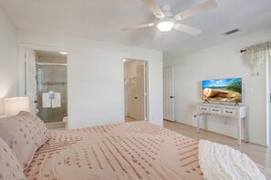 A bedroom with a bed, a ceiling fan, a TV, and a bathroom visible through an open door.