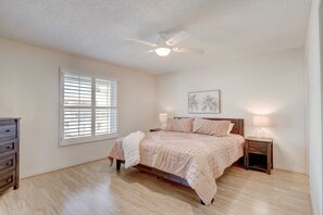 A bedroom with a bed, two bedside tables, a ceiling fan, and a window with blinds.
