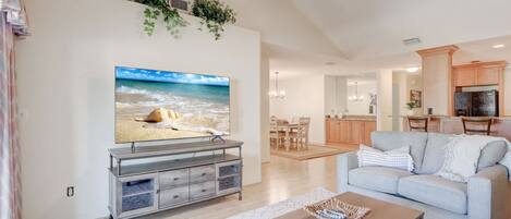 A living room with a television, a sofa, a coffee table, and a kitchen in the background.