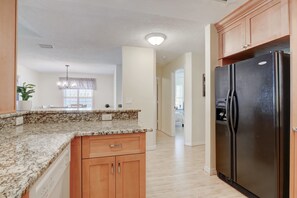 A kitchen with granite countertops, wooden cabinets, a black refrigerator, and a pendant light.