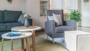 Un salon moderne avec un canapé gris, un fauteuil gris, une petite table ronde ornée d’un vase et de livres, et un meuble avec des portes en verre.
