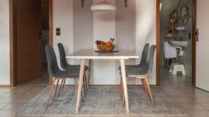 Un coin repas avec une table blanche, quatre chaises et un panier de fruits.