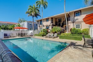 A swimming pool with lounge chairs and umbrellas, surrounded by palm trees and a building with a staircase. - A-2 - Waterfront Condo Near Naples Bay & Beaches (Naples)