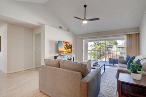 A spacious living room with a ceiling fan, a large window with a view of the outside, and a flat-screen TV mounted on the wall.