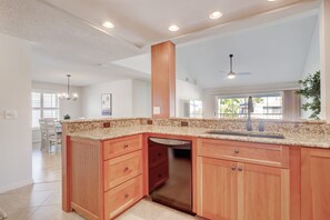 A kitchen with a granite countertop, wooden cabinets, a dishwasher, and a ceiling fan.
