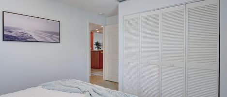 Un dormitorio con cama, un armario blanco con puertas empaneladas y un cuadro en la pared.