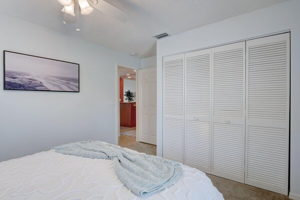A bedroom with a bed, a white closet with louvered doors, and a framed picture on the wall.