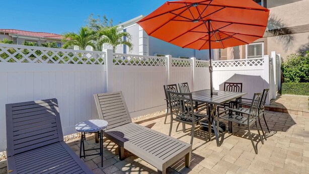 Une terrasse extérieure avec une table et des chaises, un fauteuil de relaxation et un grand parasol orange.