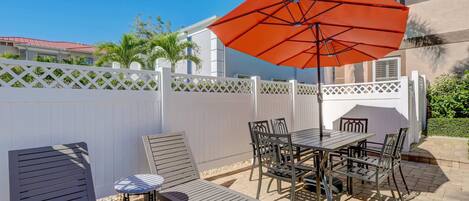 An outdoor patio with a table and chairs, a lounge chair, and a large orange umbrella.