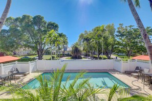 A pool area with a white fence, palm trees, and a clear blue sky.