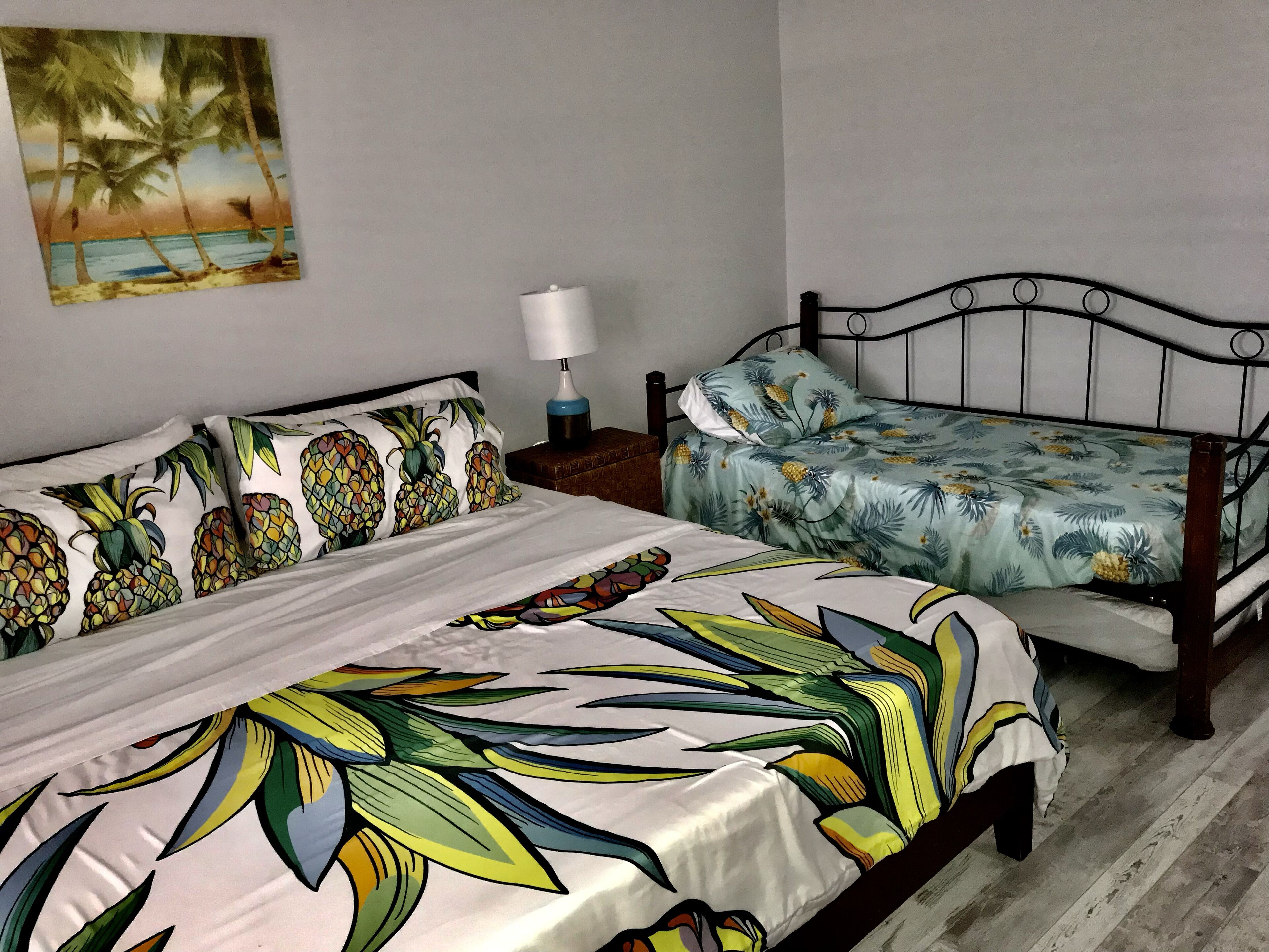 Een slaapkamer met een bed, nachtkastje, lamp en een schilderij van een strand.