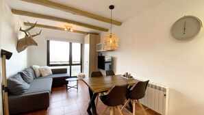 Een moderne woonkamer met een bank, een eettafel met stoelen, een televisie en een groot raam.