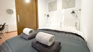 Een hotelkamer met een bed, twee wandlampen, een houten deur en twee afbeeldingen van geweië herten.
