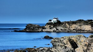A coastal house with a view of the sea, situated on rocky terrain.