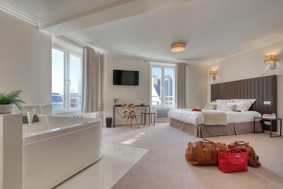 A modern hotel room with a large bed, a desk, a flat-screen TV, and a bathtub.