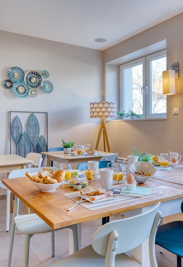 Un comedor con una mesa de madera, sillas blancas y diversas opciones para el desayuno.