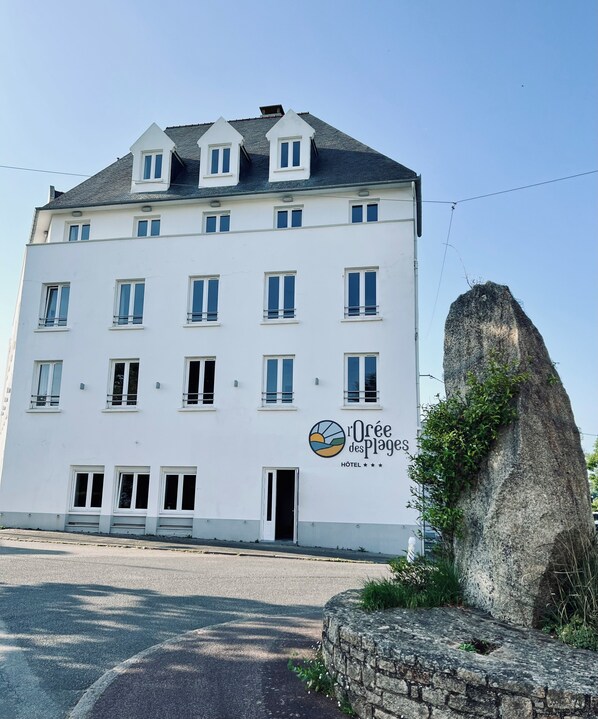A white hotel with multiple windows and a sign reading "Oure des Plages HOTEL".