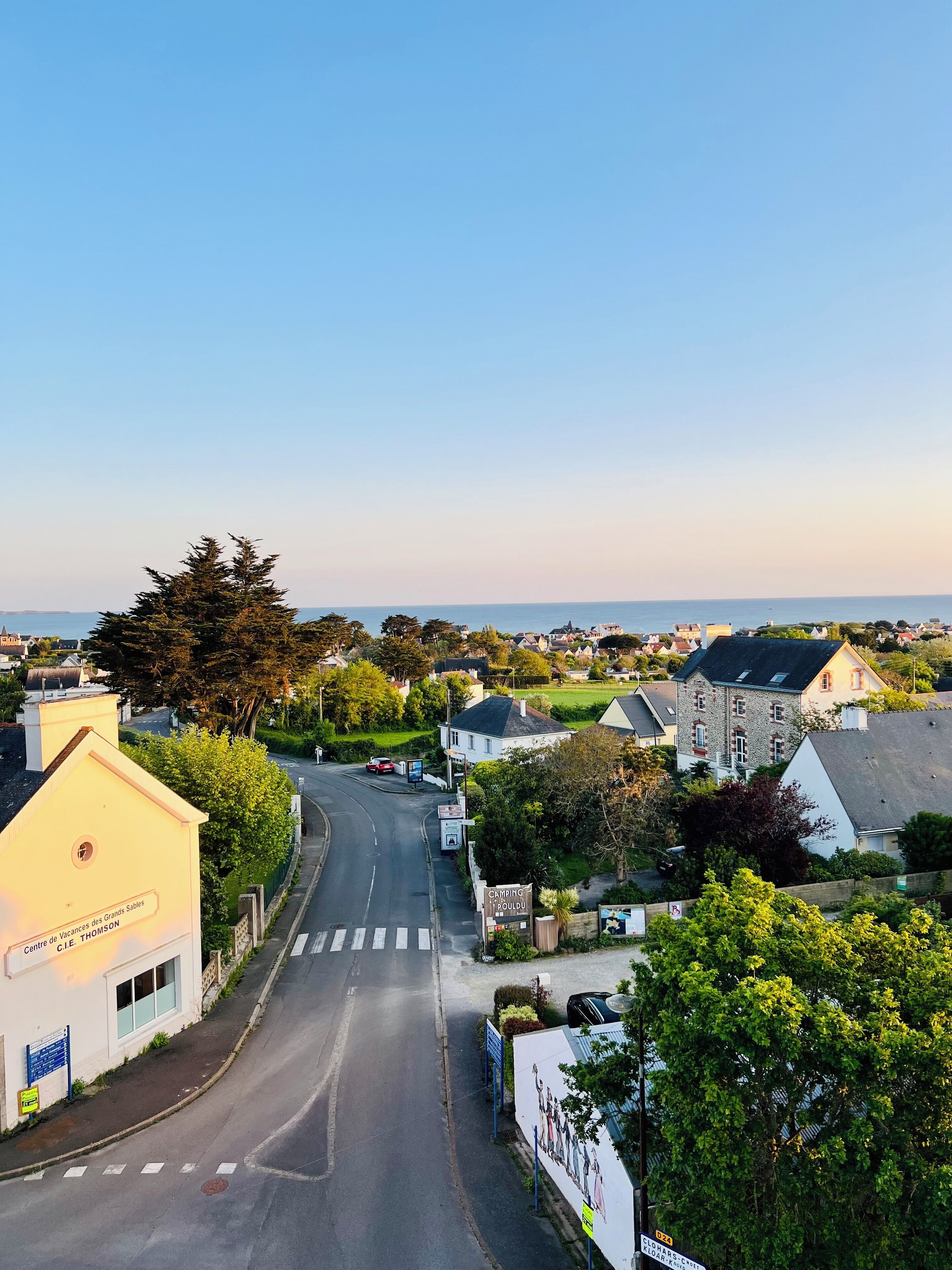 Une ville côtière, avec une route menant à un bâtiment blanc sur lequel on peut lire l’inscription « Centre de Vacances des Grands Sables C.I.E. Thomson ».