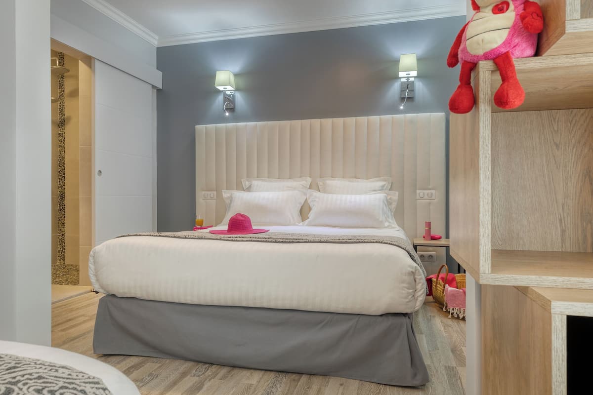 A modern bedroom with a large bed, a wooden headboard, a plush red toy, and a small shelf.