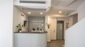 Zona de recepción con mostrador curvo, plantas en macetas y un letrero que dice "Rimini Bay Suites & Residence".