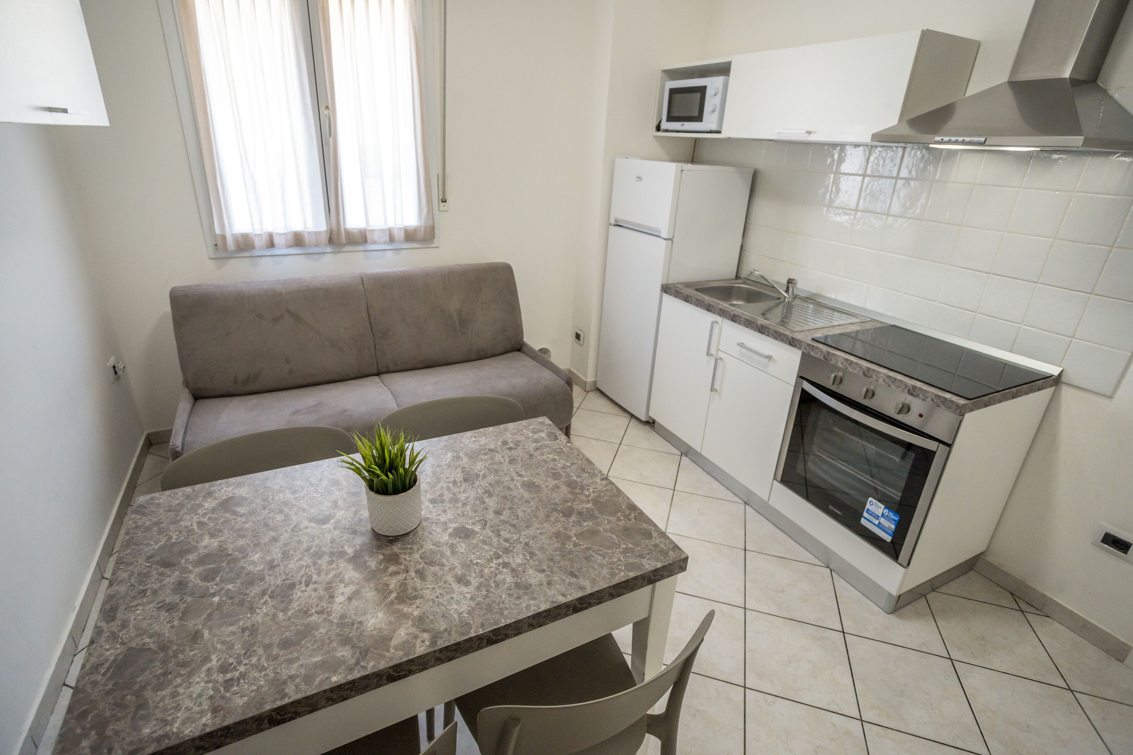 Cocina compacta con microondas, horno y lavamanos. Hay una pequeña mesa de comedor con una planta y un sofá en la esquina.