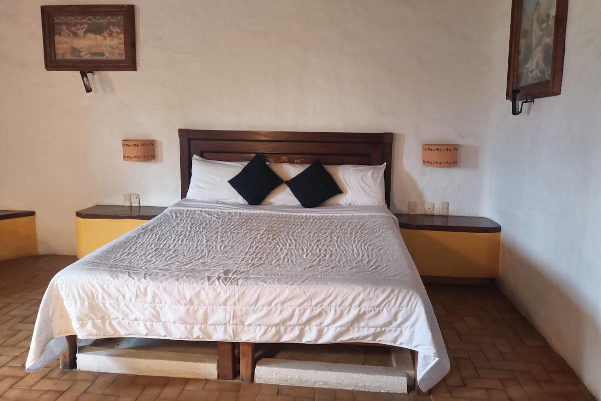 A neatly made bed with a white bedspread and two black pillows, flanked by wooden nightstands with small lamps.