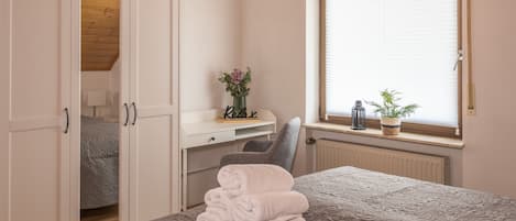 Un dormitorio con cama, escritorio, silla, radiador y ventana con persianas.