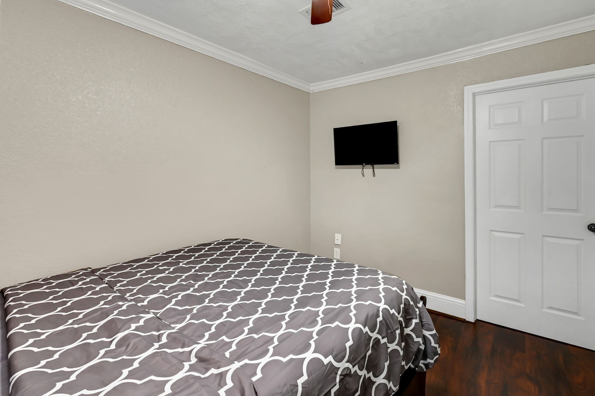 Une chambre à coucher avec un lit, un téléviseur fixé au mur et une porte blanche.