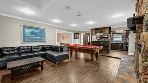 Ein Wohnzimmer mit Pooltisch, einer schwarzen Ledersofa und einer Küche im Hintergrund.