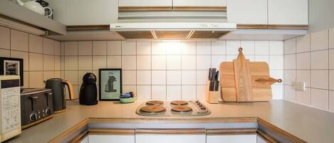 A kitchen with white cabinets, a stove, a coffee maker, and a wooden cutting board.