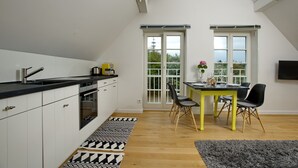 Et moderne køkken med hvide skabe, en sort bordplade, samt et spiseområde med et gult bord og sorte stole.