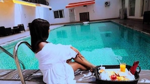 A woman sitting by an indoor pool with a tray of breakfast items.