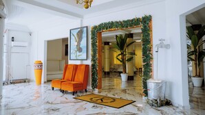 A lobby with a marble floor, a reception desk, a framed artwork, a potted plant, and a decorative archway.