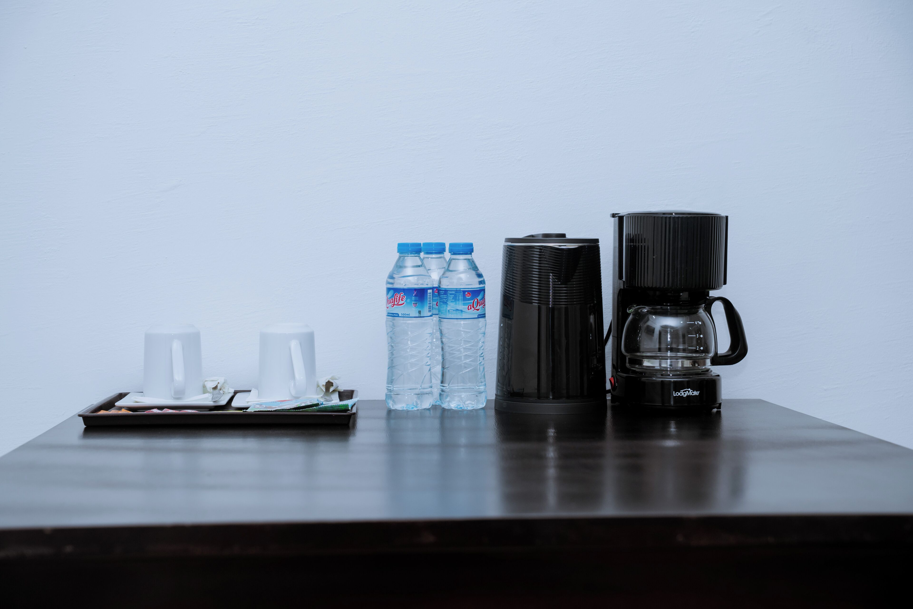Una mesa de madera oscura con una bandeja que contiene dos tazas blancas, dos botellas de agua y una cafetera.