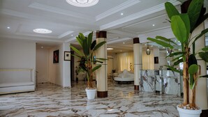 A lobby with marble flooring, large potted plants, a reception desk, and a white sofa.