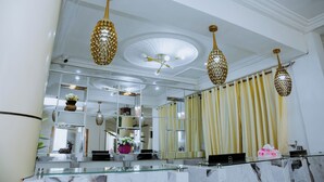 A hotel lobby with a glass reception desk, a large mirror, and decorative hanging lamps.
