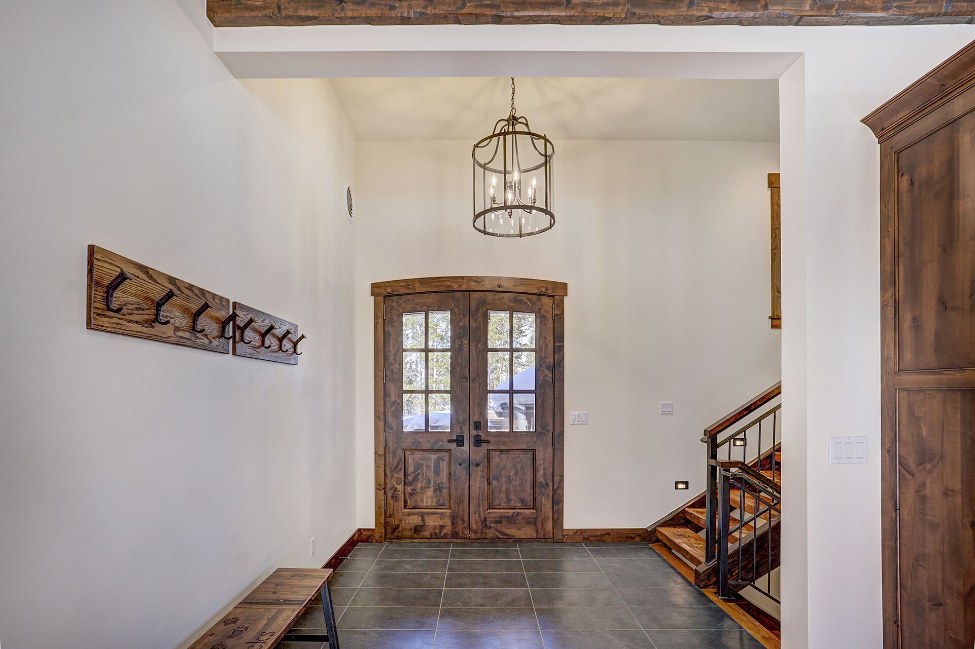 A hallway with a wooden door, a bench, and a chandelier.