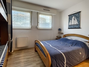 A bedroom with a bed, a window, a radiator, and a wall-mounted shelf.
