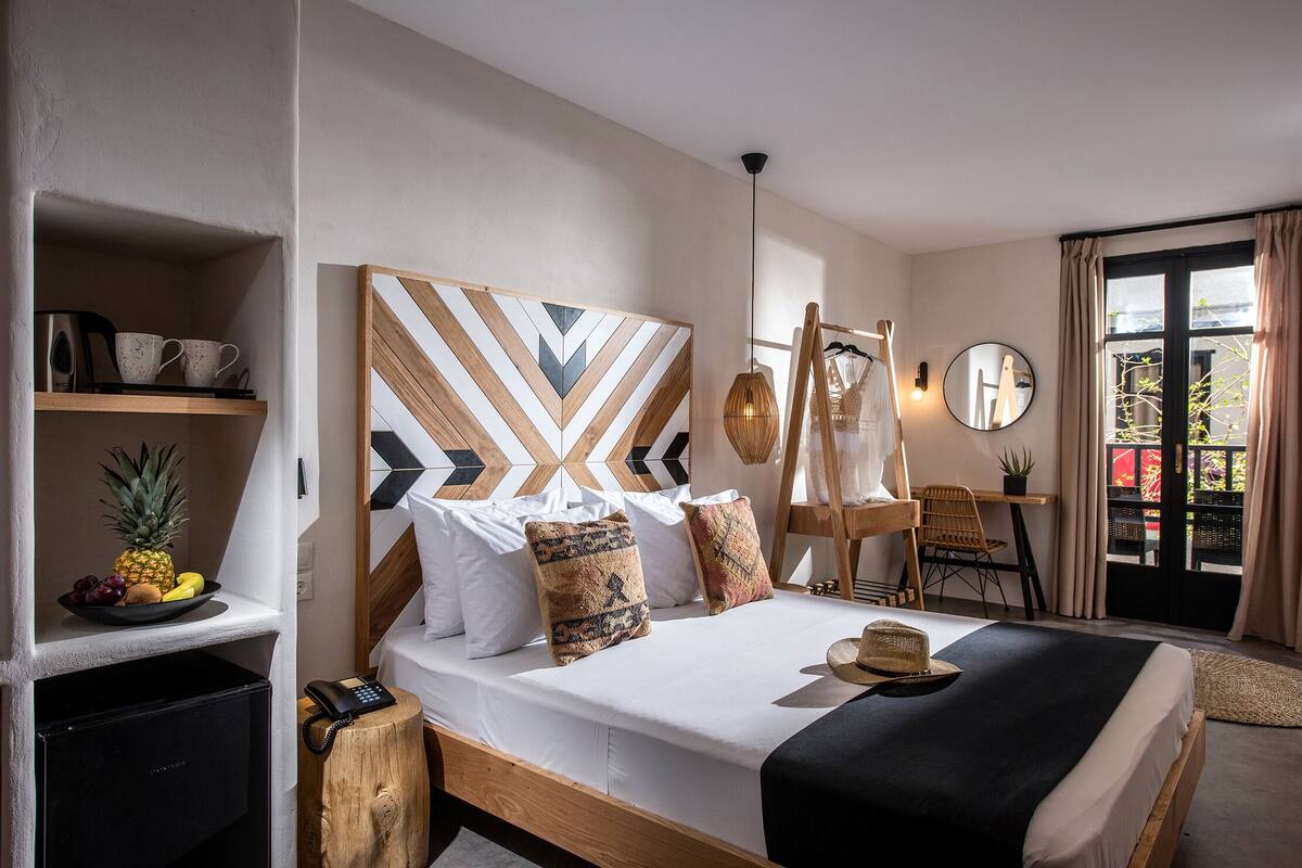 A neatly arranged hotel room with a bed, a small desk, a chair, and a view of the outside.