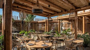 An outdoor dining area with wooden tables and chairs, surrounded by plants and a wooden fence. - Indigo Inn Casa - Adults Only (Hersonissos)
