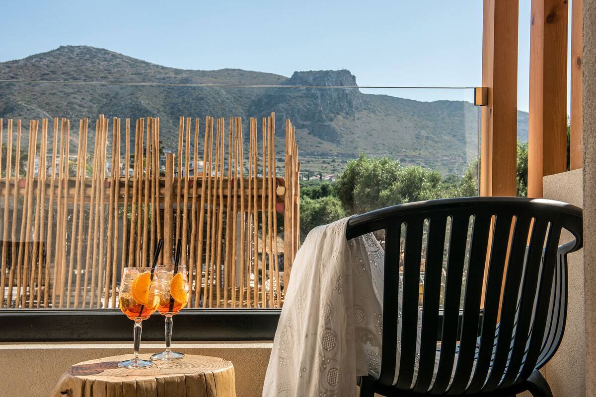 A balcony with a wooden fence, two glasses of drink with orange slices, and a chair with a white cover.