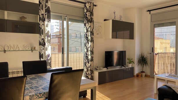 A modern living room with a dining area, a TV, and a balcony with a view of the neighborhood.