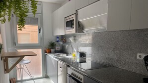 A modern kitchen with white cabinets, a granite countertop, a built-in oven, and a window with blinds.