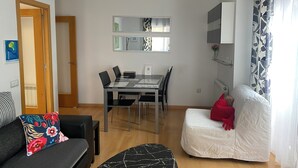 A modern living room with a dining table, a sofa, a chair, and a bed.