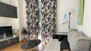 A modern living room with a black sofa, a small round table, a TV, and a patterned curtain.