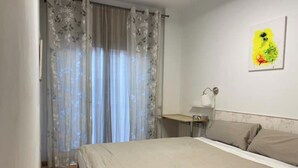 A bedroom with a bed, a bedside table, a lamp, and a window with curtains.