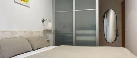 A bedroom with a bed, a wardrobe, a mirror, and a painting on the wall.