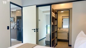 A modern hotel room with a bed, a wardrobe, and a view of a kitchen and bathroom through an open door.